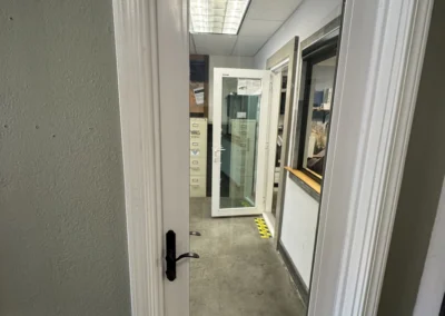 Clear glass door framed in white, leading to a brightly lit office space with another open door in the background.